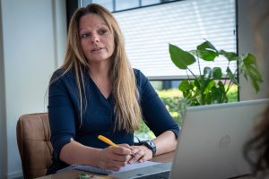 Medisch secretaresse zit aan een bureau met notitieblok en laptop tijdens een gesprek.